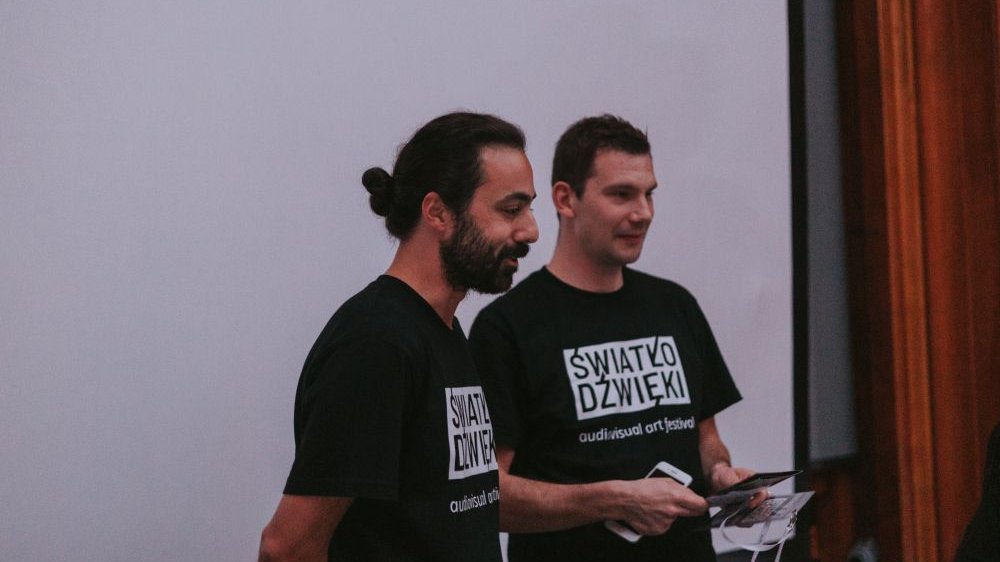 Dwóch młodych mężczyzn w czarnych festiwalowych koszulkach.
