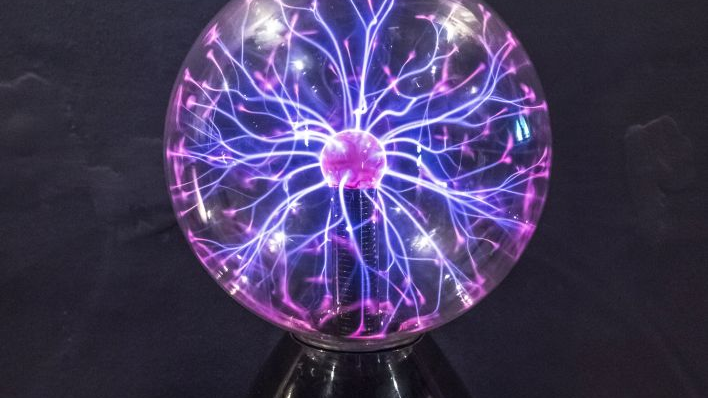 Eksponat - szklana kula z drgającymi wewnątrz fioletowymi i różowymi promieniami świateł, odchodzącymi od jednego źródła w centrum.