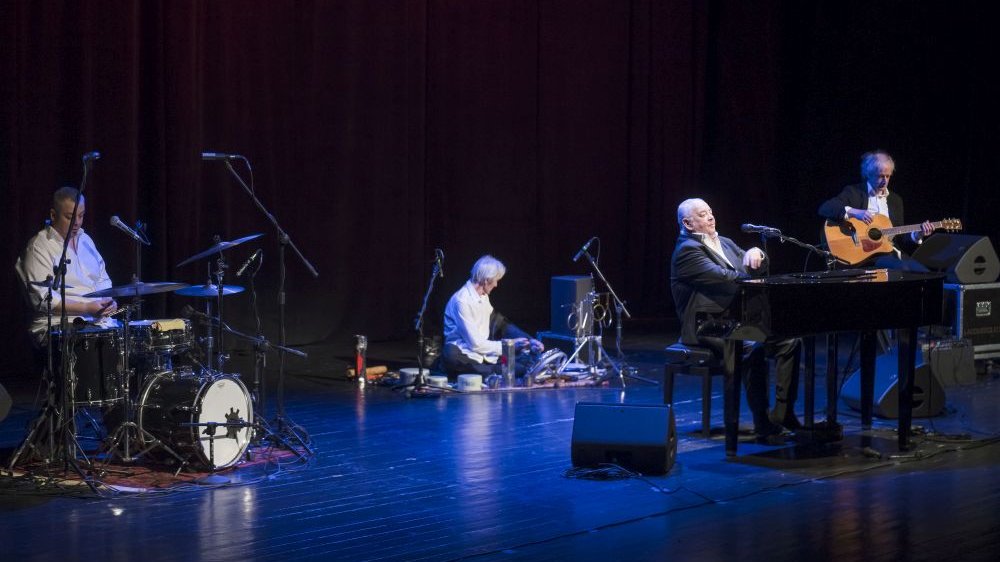Czterech muzyków na scenie. Grają od lewej na: perkusji, perkusjonaliach, fortepianie i gitarze.