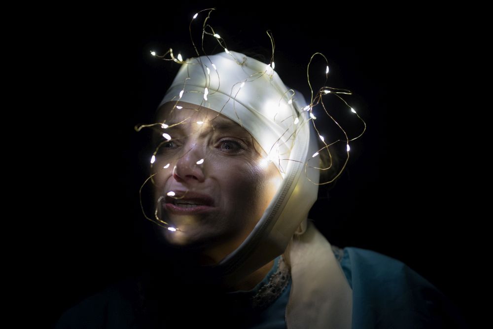 Kobieta w białym bandażu na głowie i z lampkami choinkowymi na nim robi zbolałą minę. - grafika artykułu