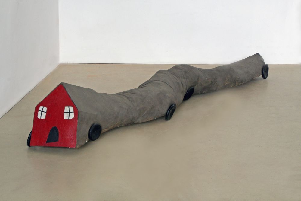 Pluszowy czerwono-szary dom na kółkach leży na podłodze galerii. - grafika artykułu