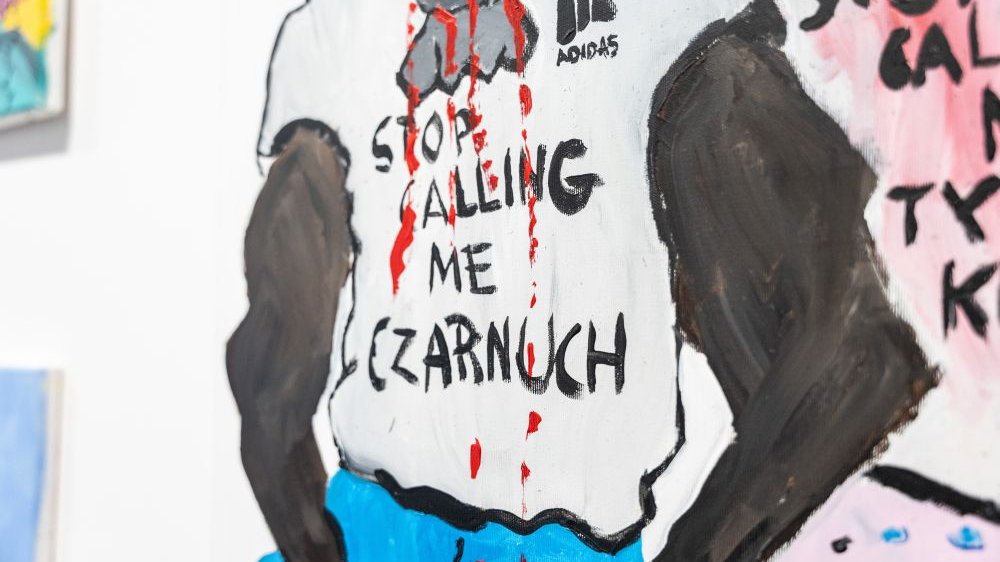 Fragment rysunku, na którym widać tors czarnoskórego mężczyzny, który ma na sobie białą koszulkę z hasłem "stop calling me czarnuch" (przestań nazywać mnie czarnuch).